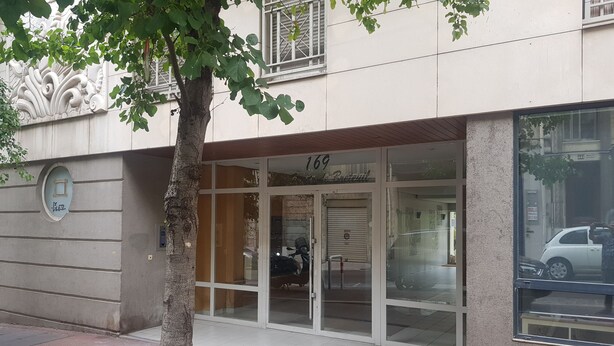 A building with a large glass entrance, a tree in front, and a number 169 sign above the door.