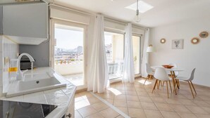 A modern kitchen with a sink and stove, a dining area with a table and chairs, and large windows with curtains.