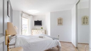 A bedroom with a bed, bedside table, lamp, dresser, TV, and decorative wall panels.
