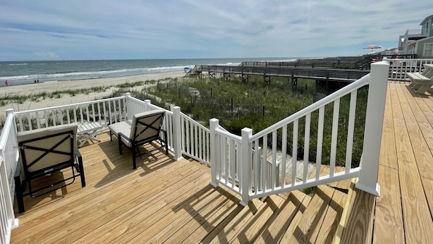 Eine Holzterrasse mit weißen Geländern mit Blick auf einen Strand und eine Promenade.