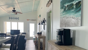 Ein wohnbereich im Strandstil mit einem Esstisch, Stühlen, einer Kaffeemaschine und Blick aufs Meer.
