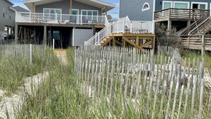 Ein Strandgrundstück mit einem zweistöckigen Haus, inklusive Balkon und Holzterrasse.