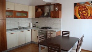 Een moderne keuken met houten kastjes, een gasfornuis en een eethoek met een tafel en stoelen.