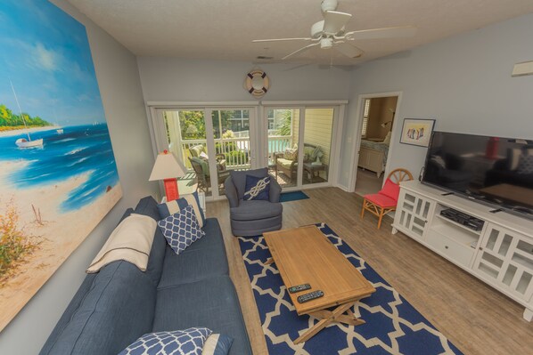 A living room with a sofa, armchairs, a coffee table, a TV, and a painting of a beach scene.
