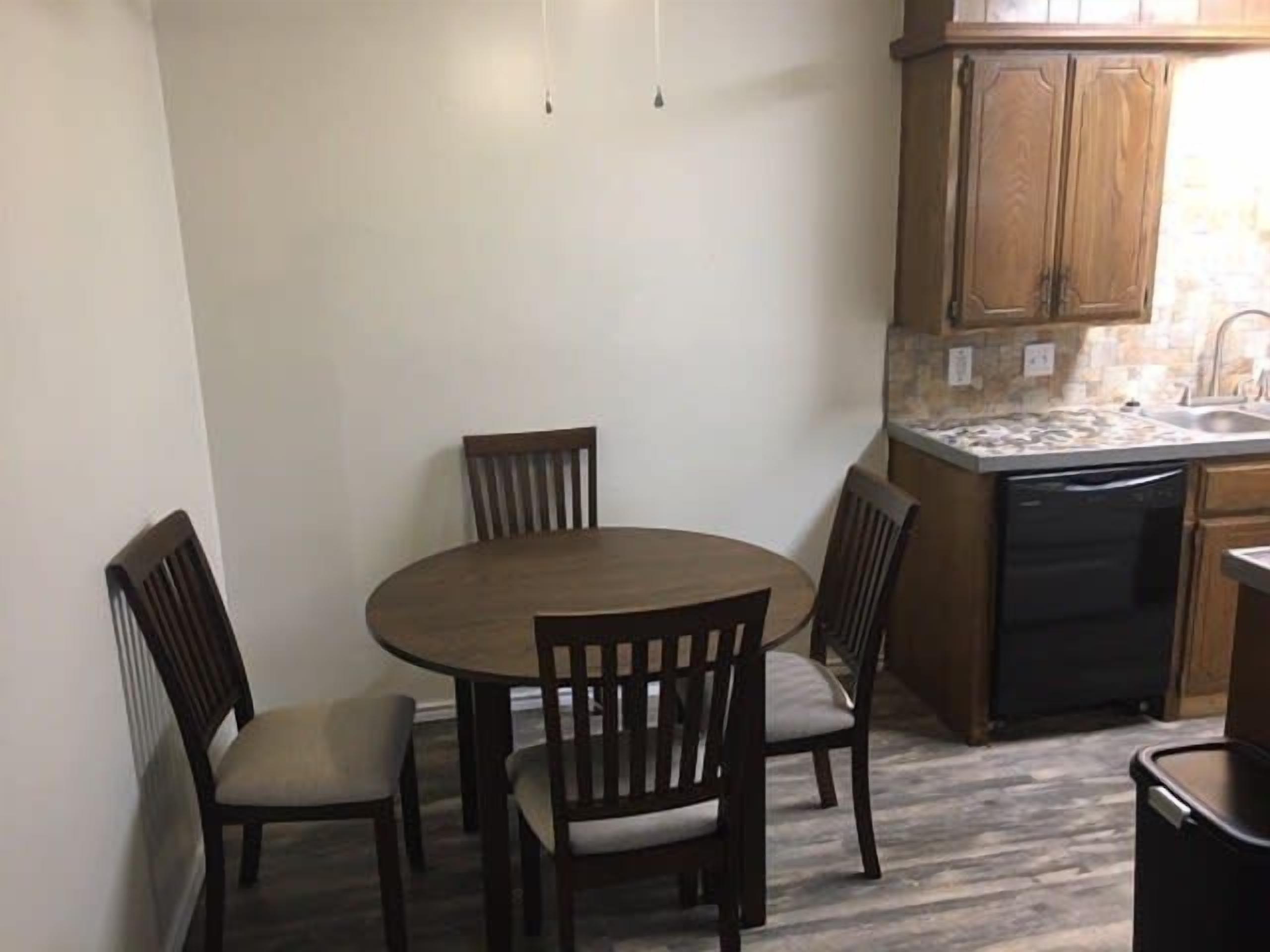Cocina compacta con mesa y sillas, armarios de madera y lavavajillas.