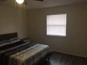 Un dormitorio con una cama, una mesita de noche, un ventanal y un ventilador de techo.