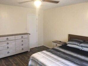A bedroom with a bed, a dresser, a nightstand, and a ceiling fan.