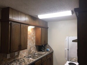 A compact kitchen with wooden cabinets, a granite countertop, a sink, and a white refrigerator.