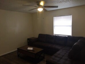 A living room with a dark brown sectional sofa, a small wooden coffee table, and a ceiling fan.
