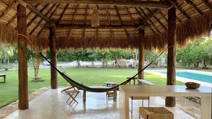 A covered outdoor area with a thatched roof, a hammock, a pool, and a table with a basket. - Boutique Resort in Mayan Jungle, Solferino, Quintana Roo (Solferino)