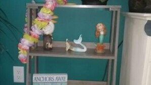 A teal wall with a metal shelf holding decorative items, a cactus-shaped box, and a sign that reads "ANCHORS AWAY". - Monthly deals ,  #4  at Beach Mirage Suites  (Brook Park)