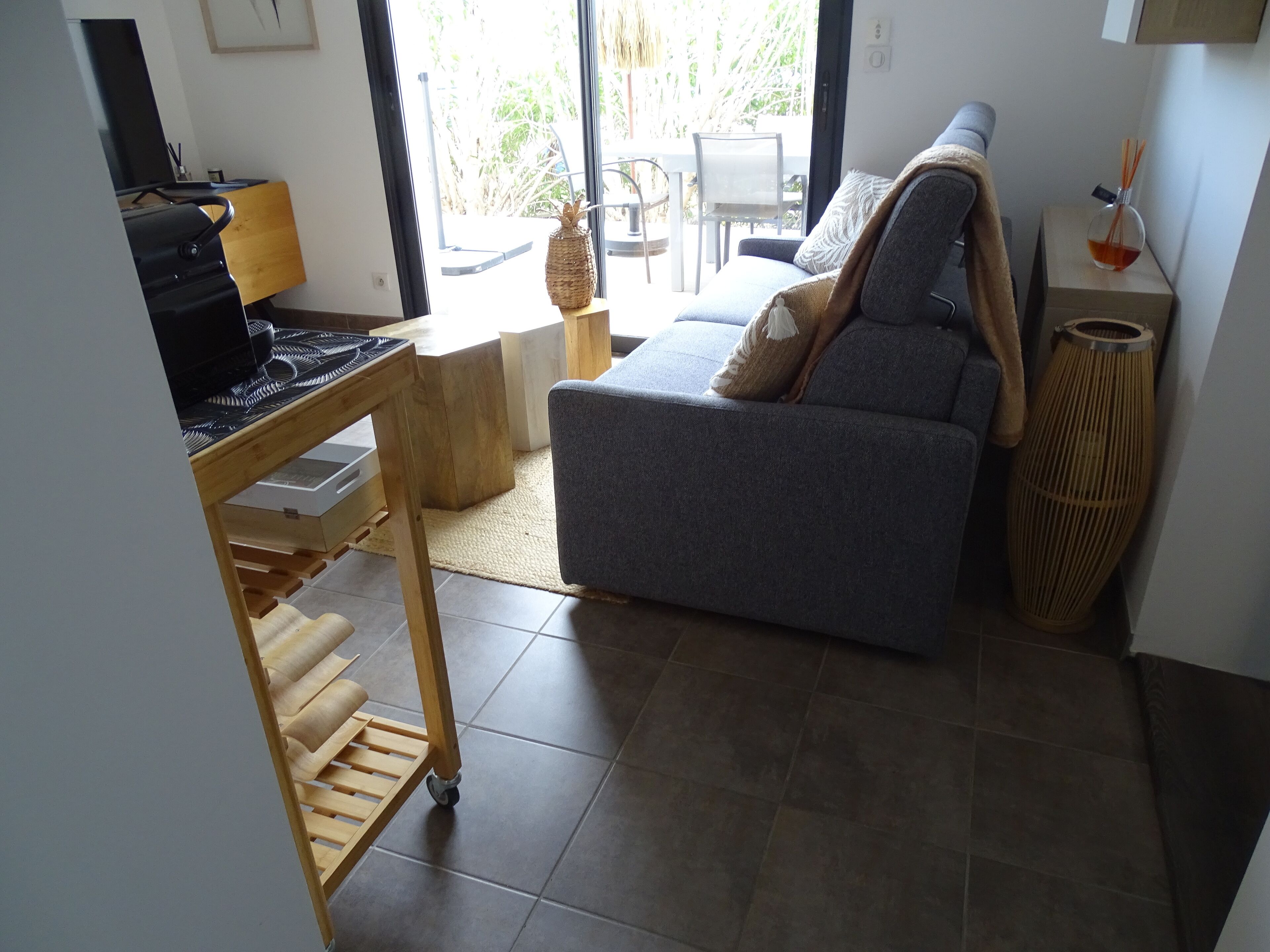 Una sala de estar con un sofá gris, una mesa de centro de madera, un televisor sobre un mueble bajo y una ventana con vista a la vegetación.