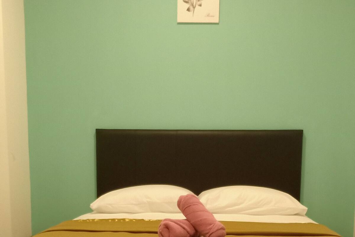 Ein Bett mit brauner Matratze, weißen Kissen, einem schwarzen Kopfteil und einer türkisblauen Wand mit einem kleinen gerahmten Bild.
