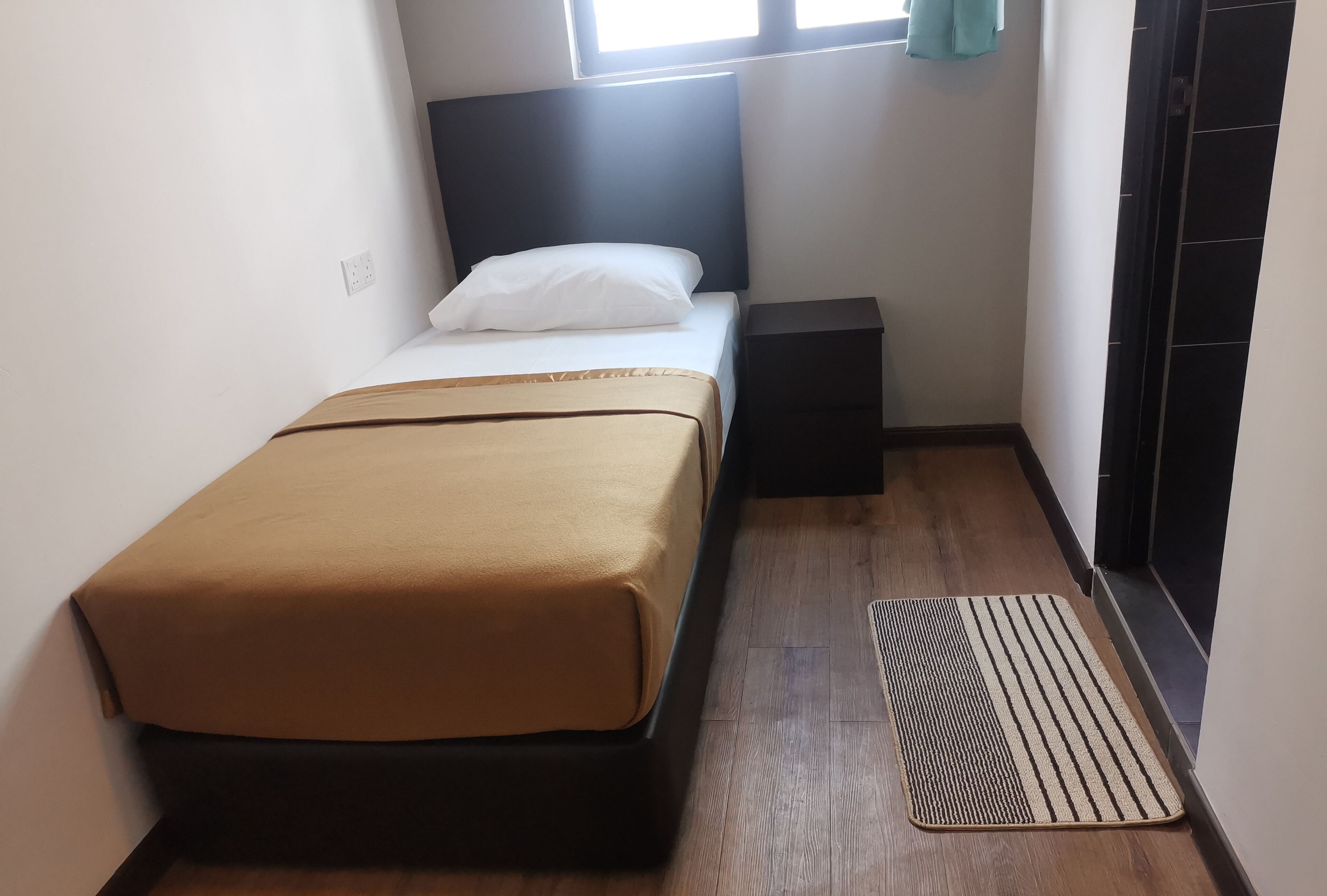 A small, neatly arranged bedroom with a single bed, a bedside table, and a window with curtains.