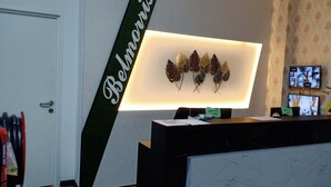 A reception desk with a computer monitor displaying a leaf decoration, a sign reading "Belmondis," and a small plant. - Belmorris Greentown Hotel (Ipoh)