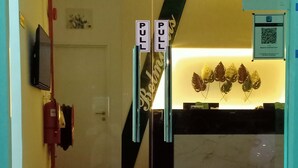 A reception area with a glass door, a fire extinguisher, a television, and a QR code sign. - Belmorris Greentown Hotel (Ipoh)