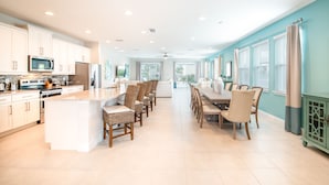 A spacious kitchen with white cabinetry, a central island, and a dining area with chairs and a table. - Vibrant Home near Disney: Private Pool, Pool Table & Waterpark - 7707GR (Kissimmee)