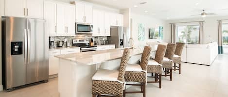 A modern kitchen with stainless steel appliances, a central island with bar stools, and a view to the outside.