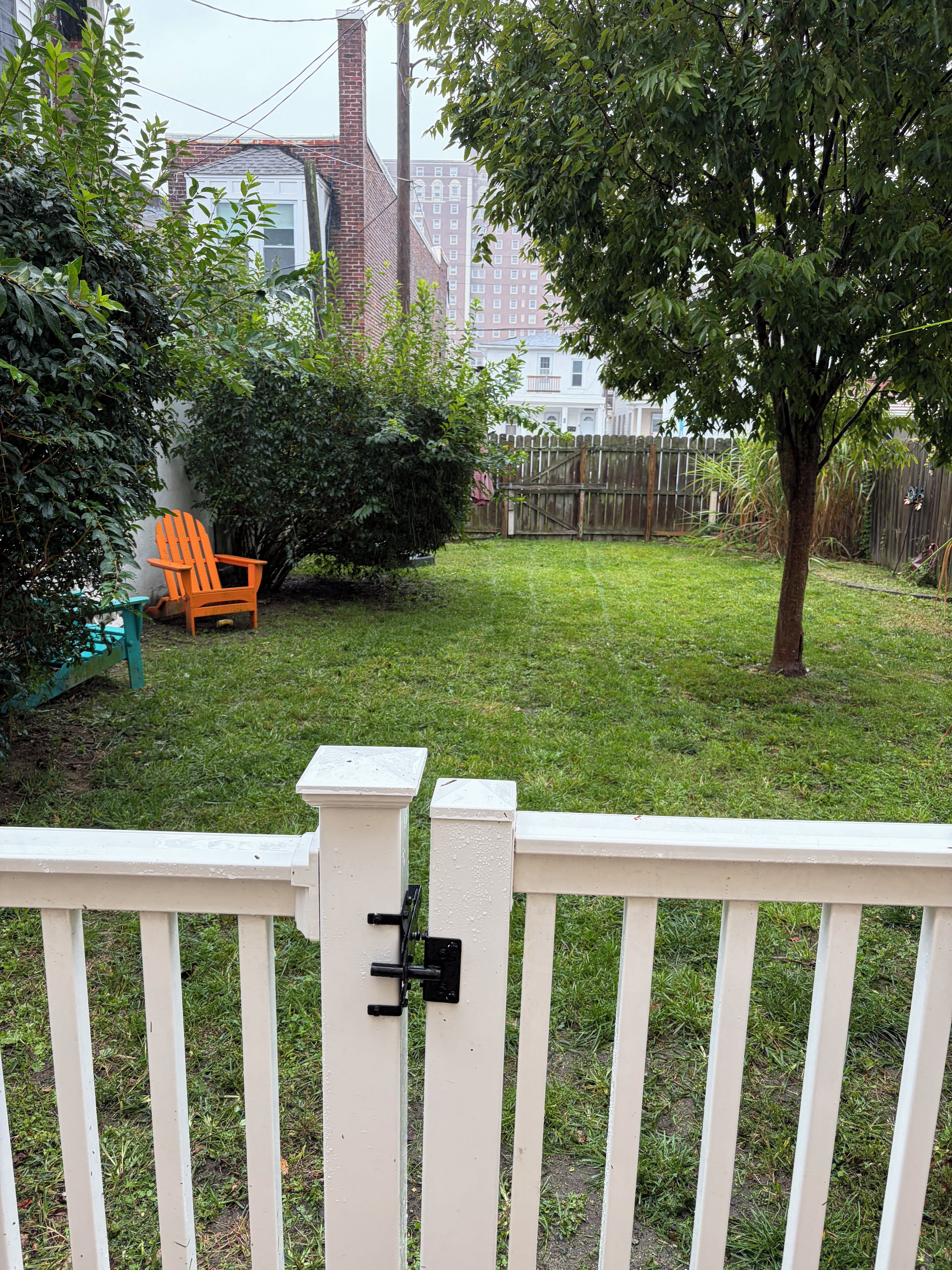 Patio trasero cercado con césped, valla de madera, un árbol y una silla.