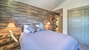 A bedroom with a wooden headboard, a bed with a light blue bedspread, two bedside lamps, a nightstand with a lamp, and a washing machine in the background. - Bozeman Stand-Alone Home w/ River Access! (Bozeman)