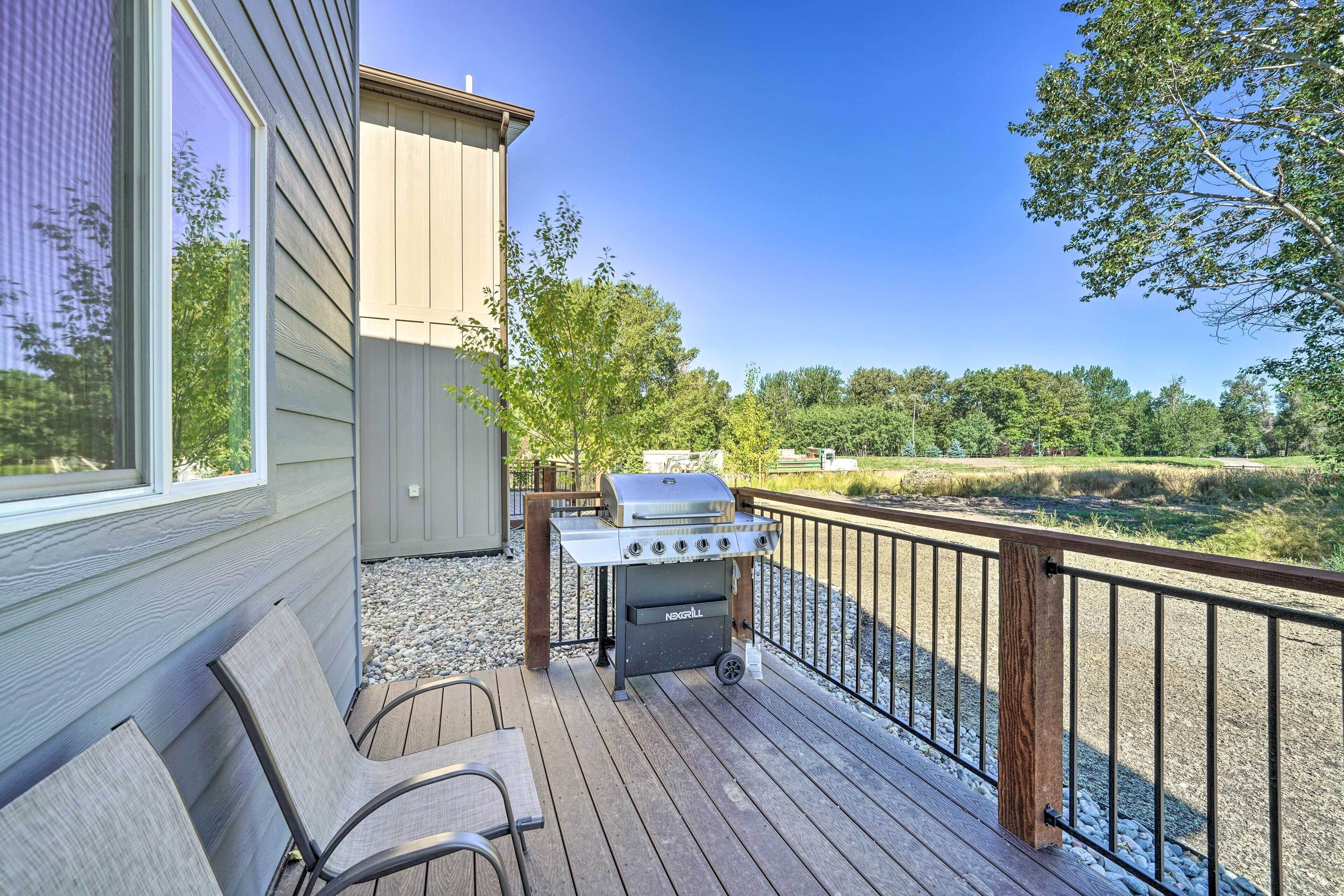 A deck with a grill, chairs, and a view of a natural landscape.