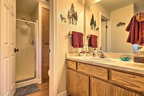 Une salle de bain avec un meuble-lavabo en bois, un évier et un miroir. Des serviettes sont accrochées au mur et il y a une porte de douche.