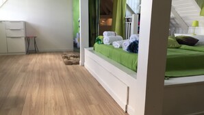 A bedroom with a wooden floor, a bed with green bedding, a small table, and a chair. - Villa Quietude (Saint François)