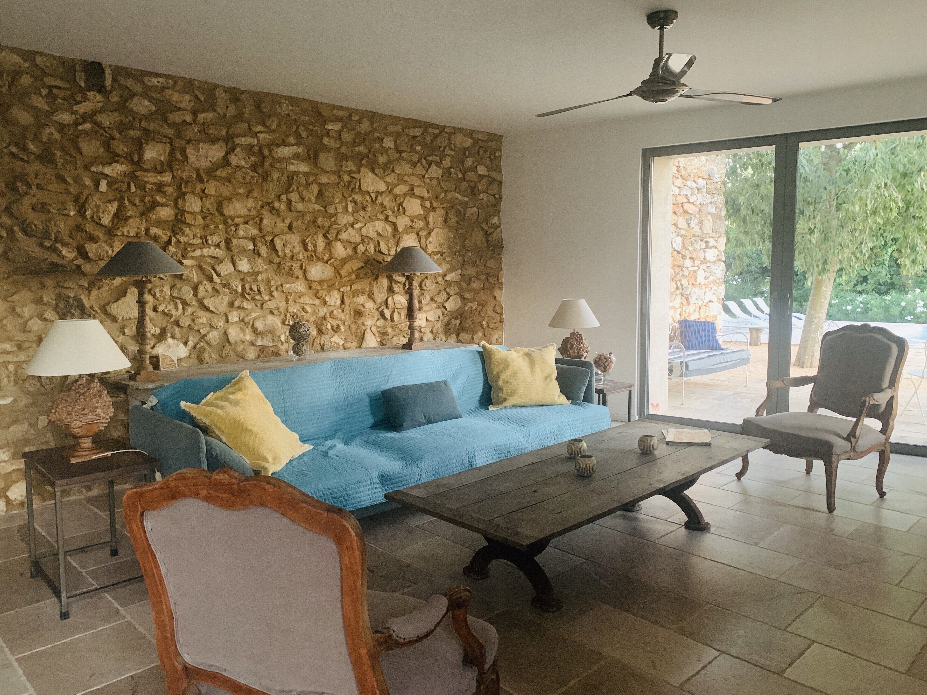A living room with a stone wall, a blue sofa, two lamps, a wooden coffee table, and a chair.