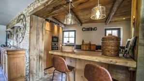 Una cocina rústica con vigas de madera, pared de piedra y una barra con taburetes.