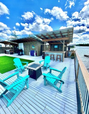 A wooden deck with outdoor seating and a bar area overlooking a body of water.