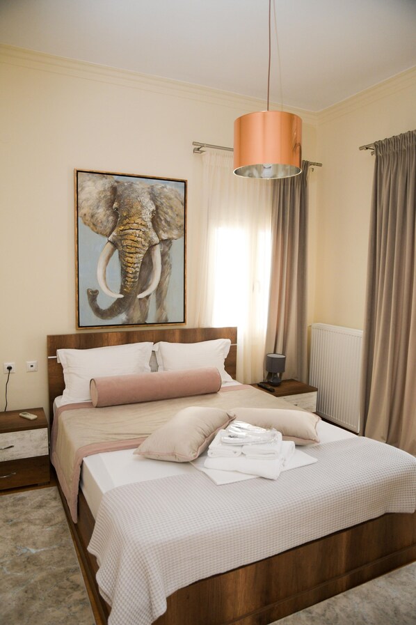 A bedroom with a wooden bed, a painting of an elephant, a hanging lamp, and a window with curtains.