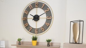 Un saló modern amb un gran televisor de pantalla plana, un rellotge decoratiu a la paret i una prestatgeria de fusta amb petites plantes.