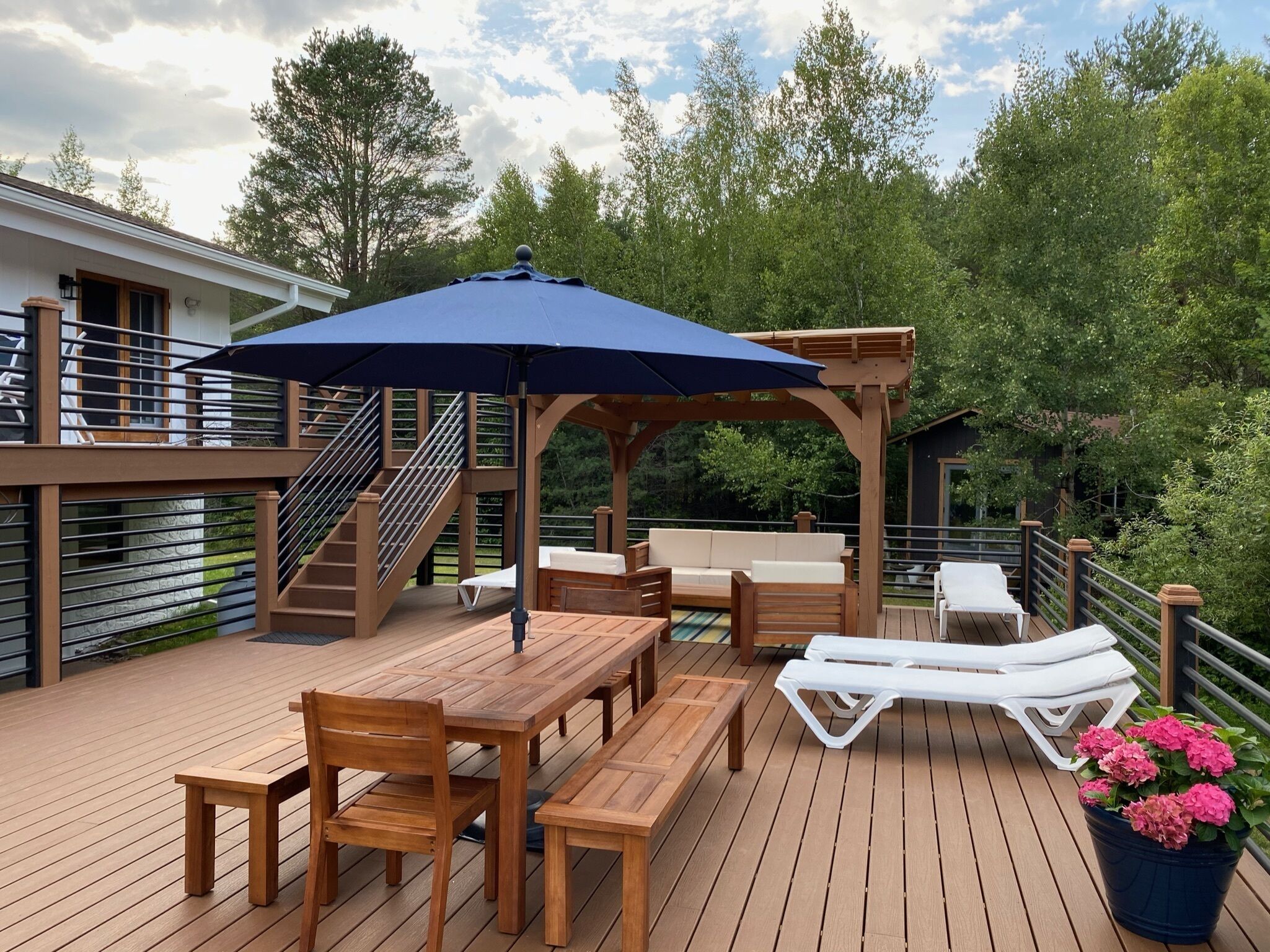 Une terrasse en bois avec une table et des chaises, un espace salon couvert et un escalier.