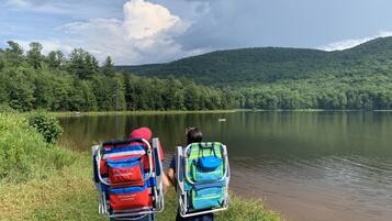 Two people with backpacks facing a lake with a forested hill in the background.