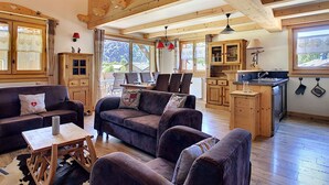 Een gezellige woonkamer met een houten plafond, een bank, een salontafel en een keukenhoek met houten kastjes en een gootsteen.