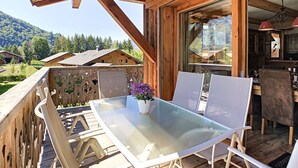 Een houten terras met een glazen tafel en stoelen, een potplant en uitzicht op het omliggende landschap.