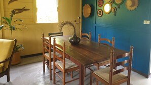 Un coin repas avec une table et des chaises en bois, un vase et des éléments de décoration murale, notamment des chapeaux et une image d’oiseau.