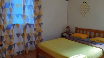 A bedroom with a bed, wooden headboard, yellow pillows, a nightstand, and a geometric-patterned curtain.