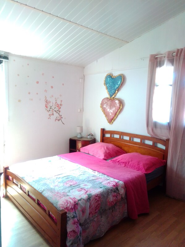 A bedroom with a wooden bed, pink bedding, a floral bedspread, and two heart-shaped wall decorations.