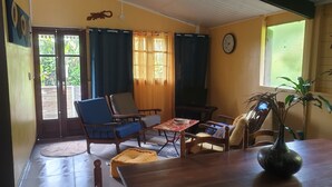 Un salon chaleureux avec une table en bois, deux chaises bleues, un fauteuil en forme de poire jaune et une plante en pot.