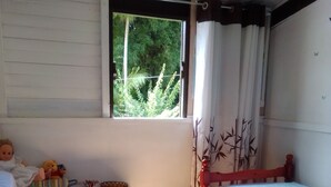 Une chambre avec deux lits, une fenêtre avec des rideaux, une étagère avec des livres et un ours en peluche, et un plancher en bois.