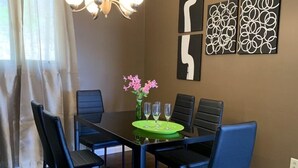 A dining area with a table set for six, surrounded by black chairs, a chandelier, and abstract wall art. - Lake George Guesthouse (Lake George)