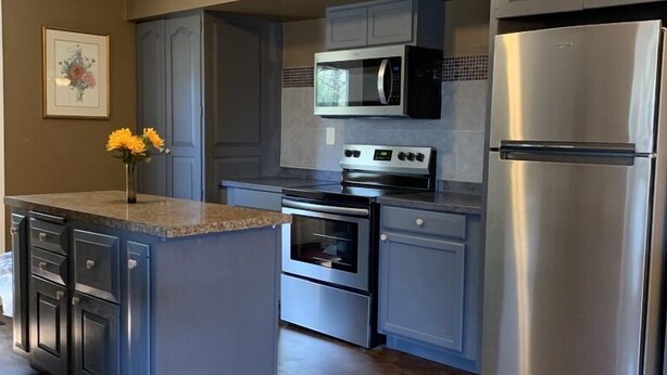 A modern kitchen with grey cabinets, a stainless steel refrigerator, a microwave, and an oven. - Lake George Guesthouse (Lake George)