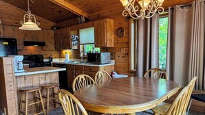 Interior de una cabaña de madera con comedor, cocina y una araña.