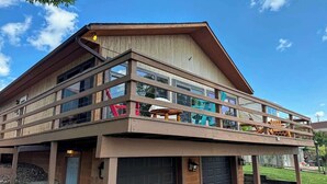 Un edificio de dos pisos con fachada de madera, ventanas amplias y un balcón con mobiliario exterior.