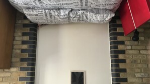 A room with a white wall, a black framed picture, and a brick-patterned wall. There are two white lamps on either side of the picture. - Cozy room in a riverside apartment (London)