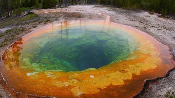 Uma grande nascente termal circular com água cristalina e um degradê de cores do verde para o laranja.