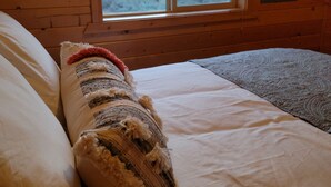 Une chambre dans un chalet en bois, avec un lit, une fenêtre donnant sur des arbres et des montagnes, et un panneau mural en bois.