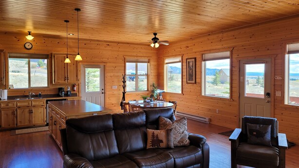 Un chalet confortable avec un intérieur en bois, un coin repas, un canapé en cuir et de grandes fenêtres offrant une vue panoramique.