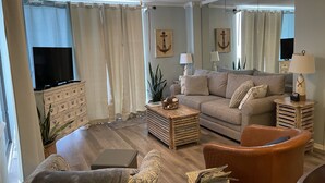 Een woonkamer met een bank, fauteuil, salontafel, televisie en decoratieve accessoires.